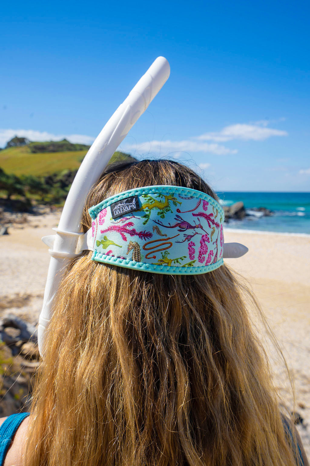 Blonde haired woman seen close up from behind at the beach with the seahorse green design neoprene mask strap tamer ocean illustration by Diver Mon Art 