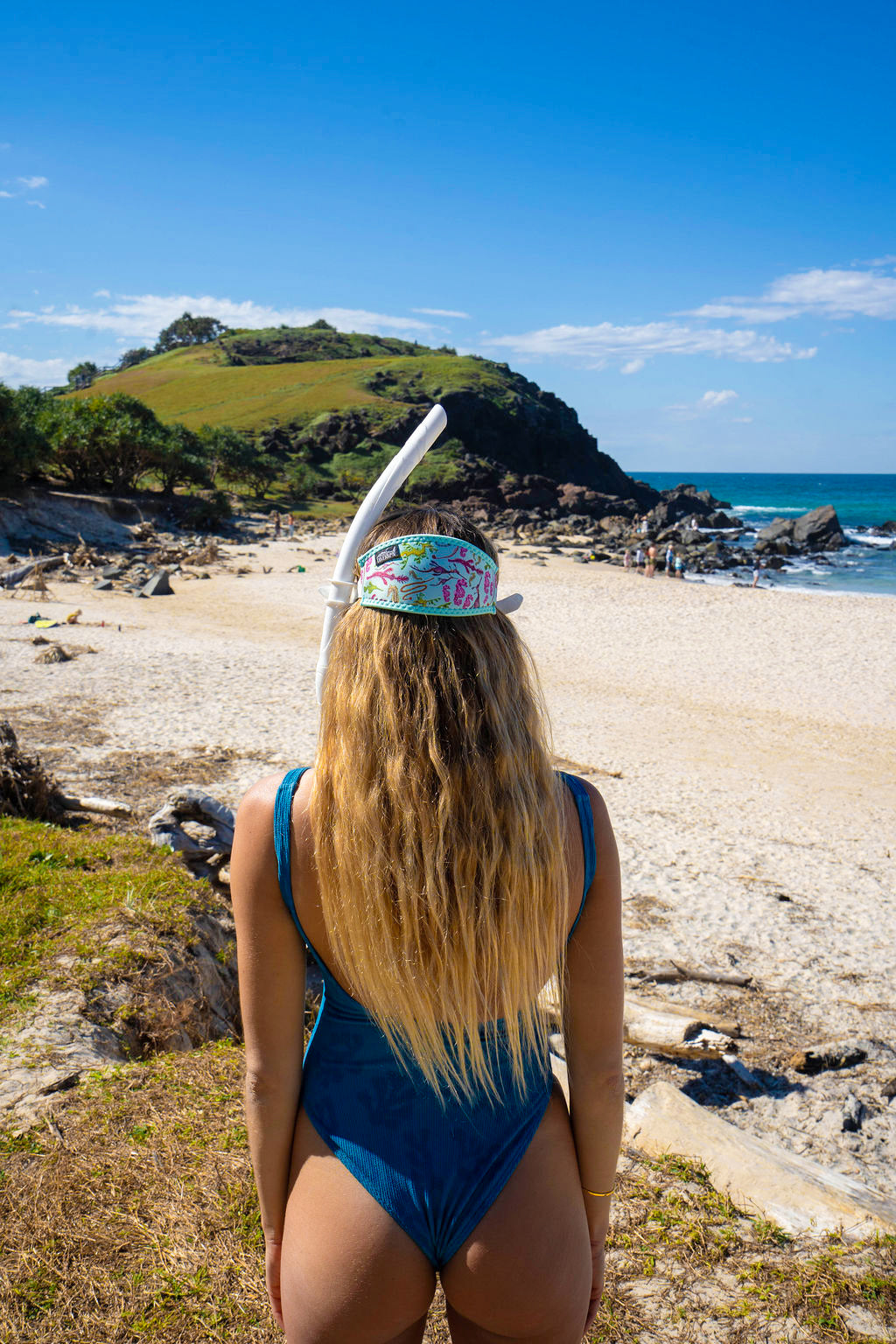 Blonde haired woman seen from behind at the beach with the seahorse green design neoprene mask strap tamer ocean illustration by Diver Mon Art