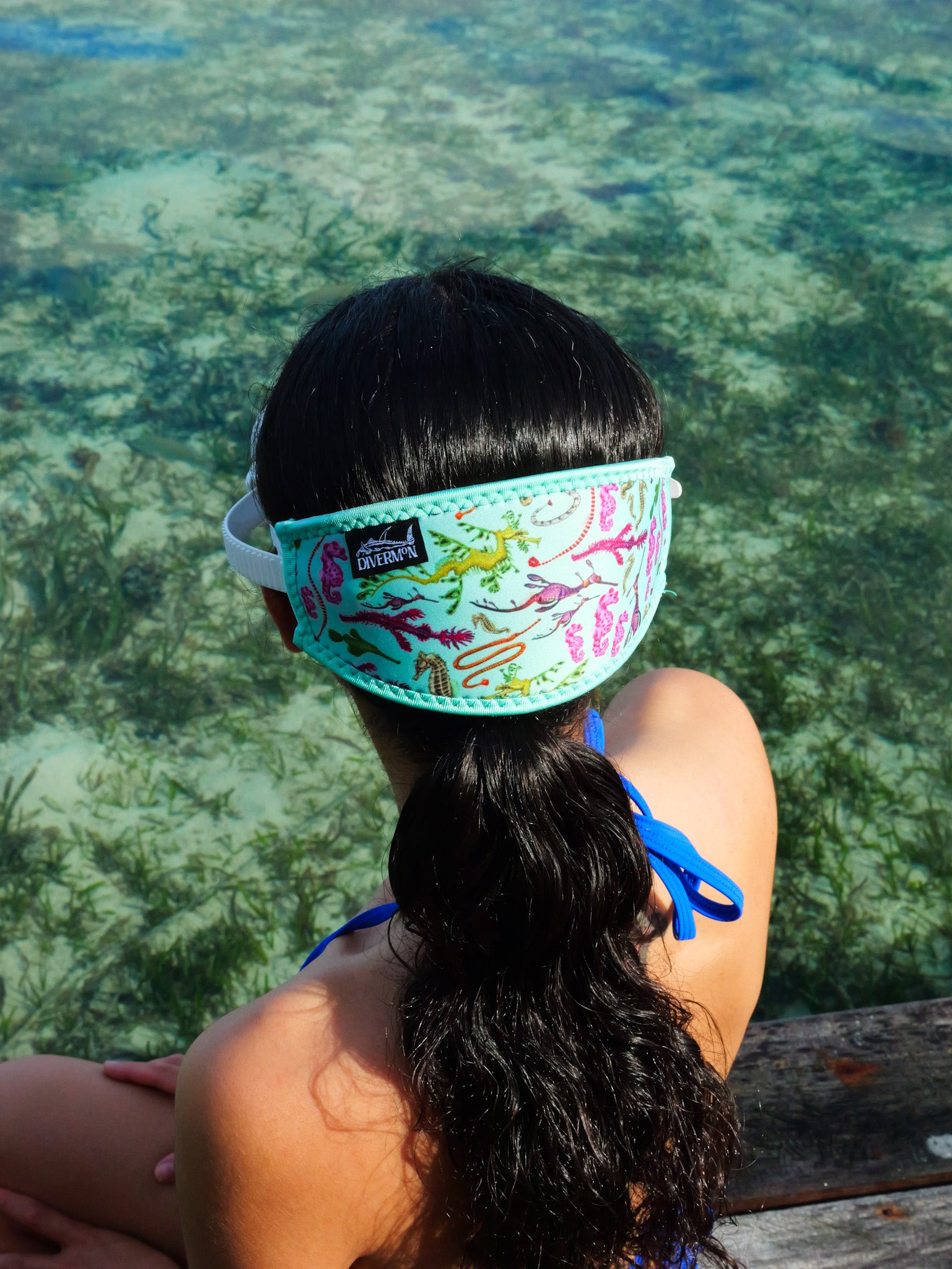 Dark haired woman shown from behind in blue clear water close up seahorse green design neoprene mask strap tamer ocean illustration by Diver Mon Art