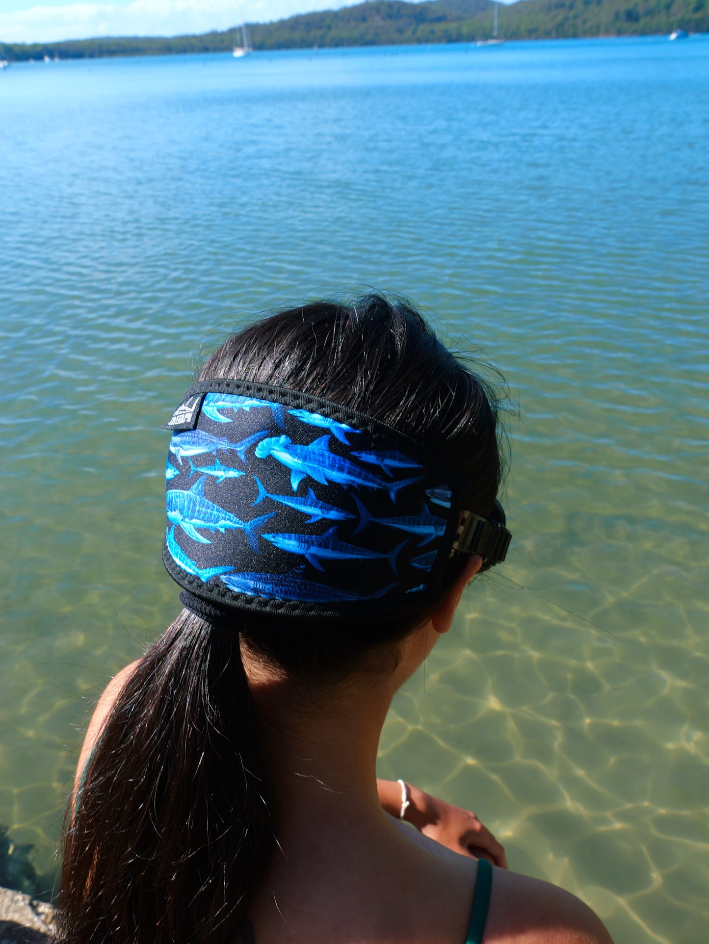 Dark haired woman shown from behind side view in blue clear water close up fitted to mask shark black design neoprene mask strap tamer ocean illustration by Diver Mon Art  