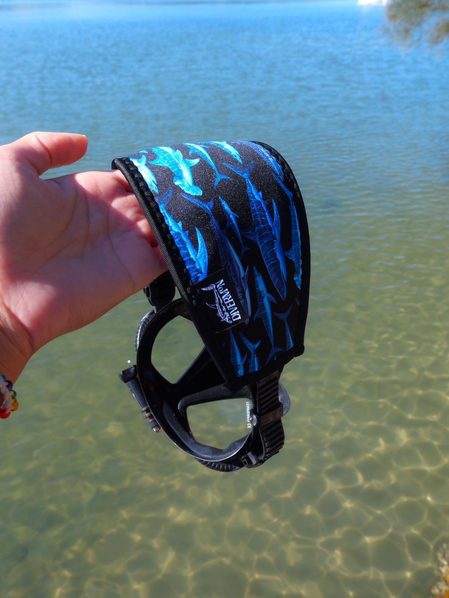 Hand holding shark black neoprene mask tamer design with clear water background fitted to mask close up details ocean illustration by Diver Mon Art