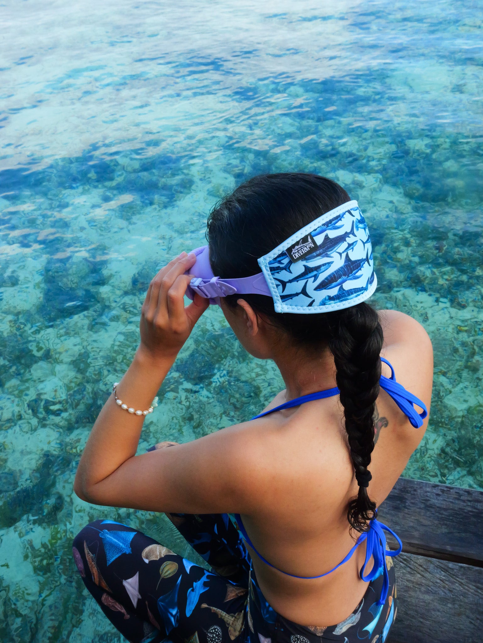 Dark haired woman shown from behind in blue clear water close up with the shark design with a light blue background neoprene mask strap tamer ocean illustration by Diver Mon Art