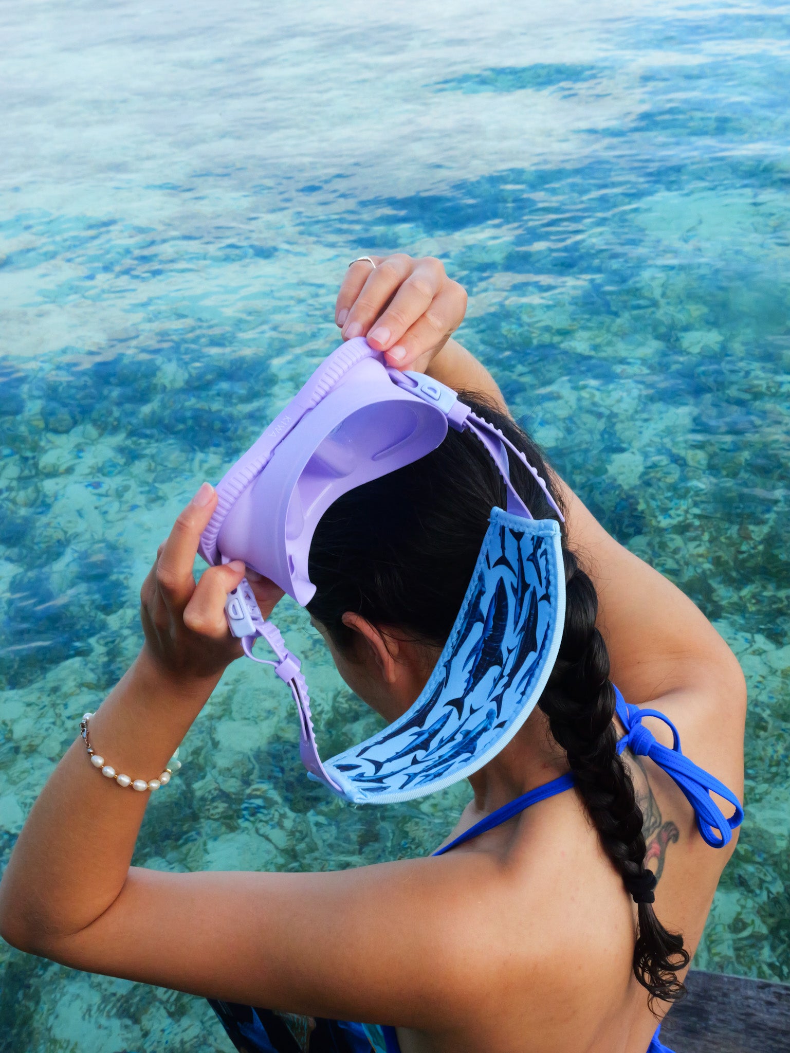 Dark haired woman seen from behind in clear blue water light blue shark design neoprene mask strap tamer tamer fitter taking off mask ocean illustration by Diver Mon Art 