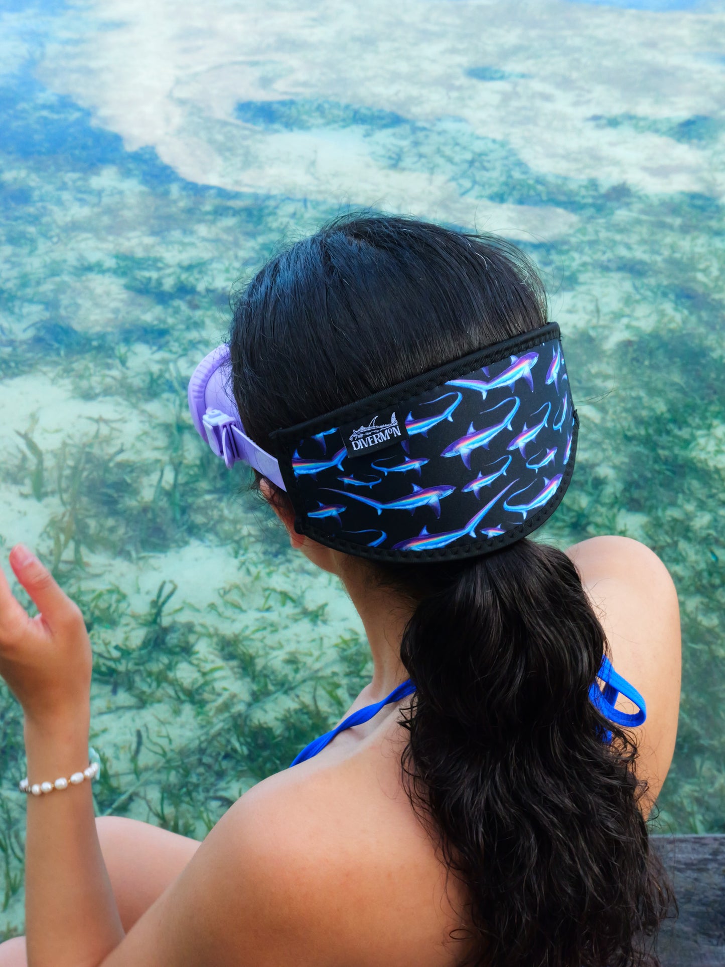 Dark haired woman shown from behind in blue clear water close up wearing a mask fitted with thresher black design neoprene mask strap tamer ocean illustration by Diver Mon Art