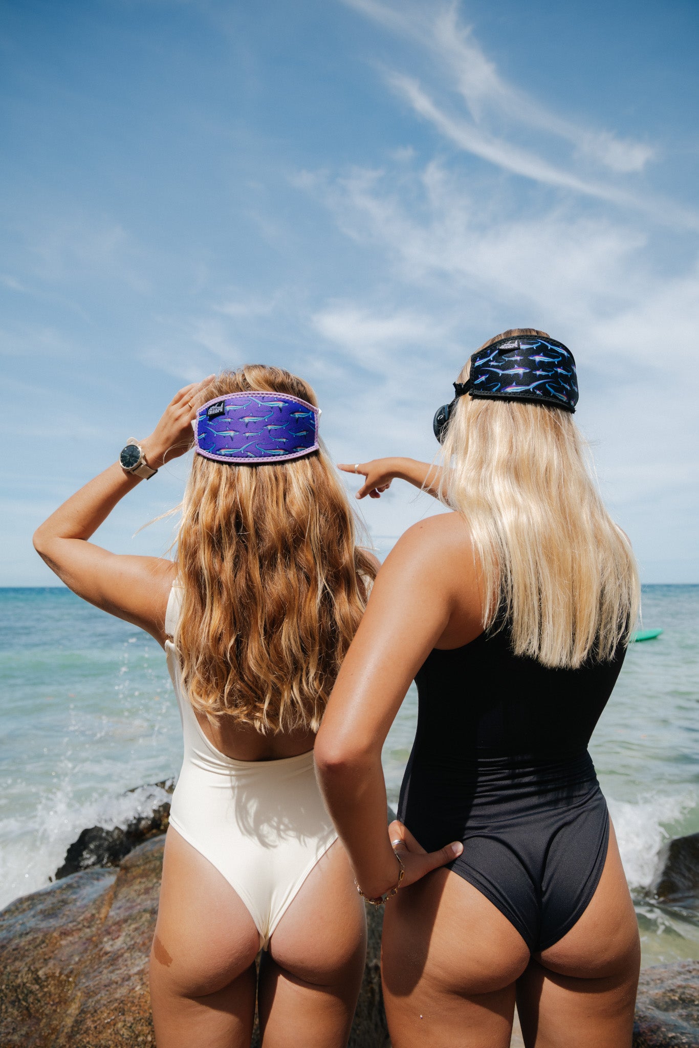 Two light haired women shown from behind by the ocean on rocks pointing wearing a mask with the limited addition black and purple thresher neoprene mask tamer ocean illustration by Diver Mon Art 