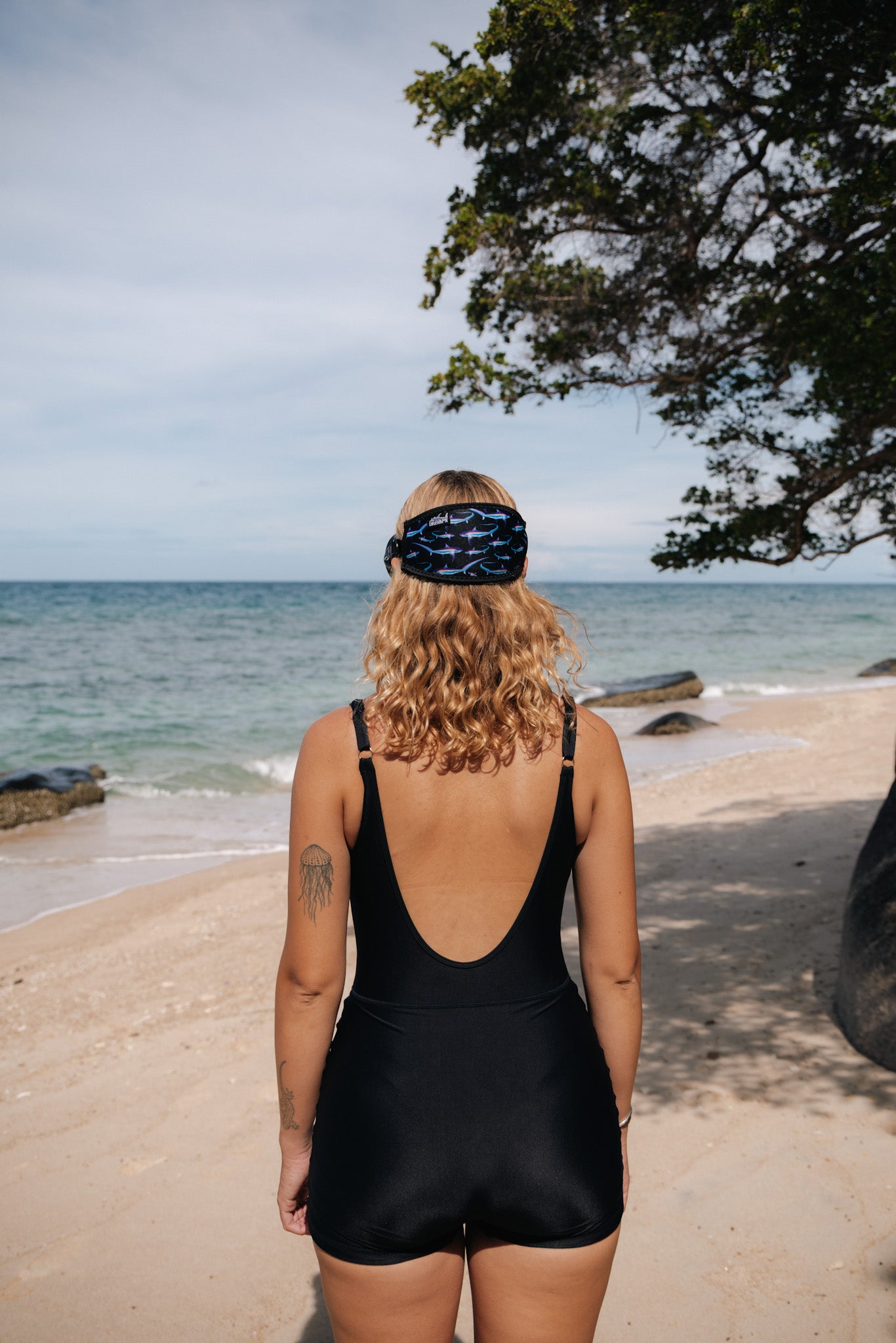 Blonde haired woman seen from behind at the beach with the thresher black design neoprene mask strap tamer ocean illustration by Diver Mon Art