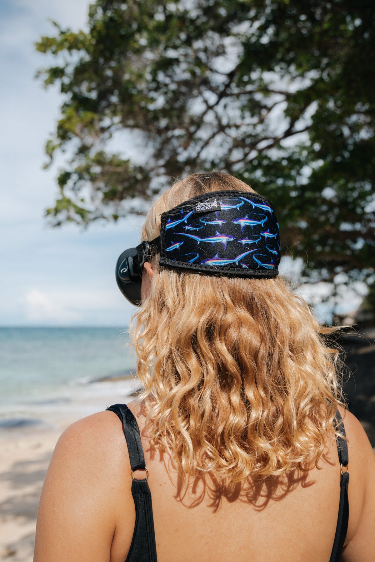 Blonde haired woman seen close up from behind at the beach with the black thresher design neoprene mask strap tamer ocean illustration by Diver Mon Art 