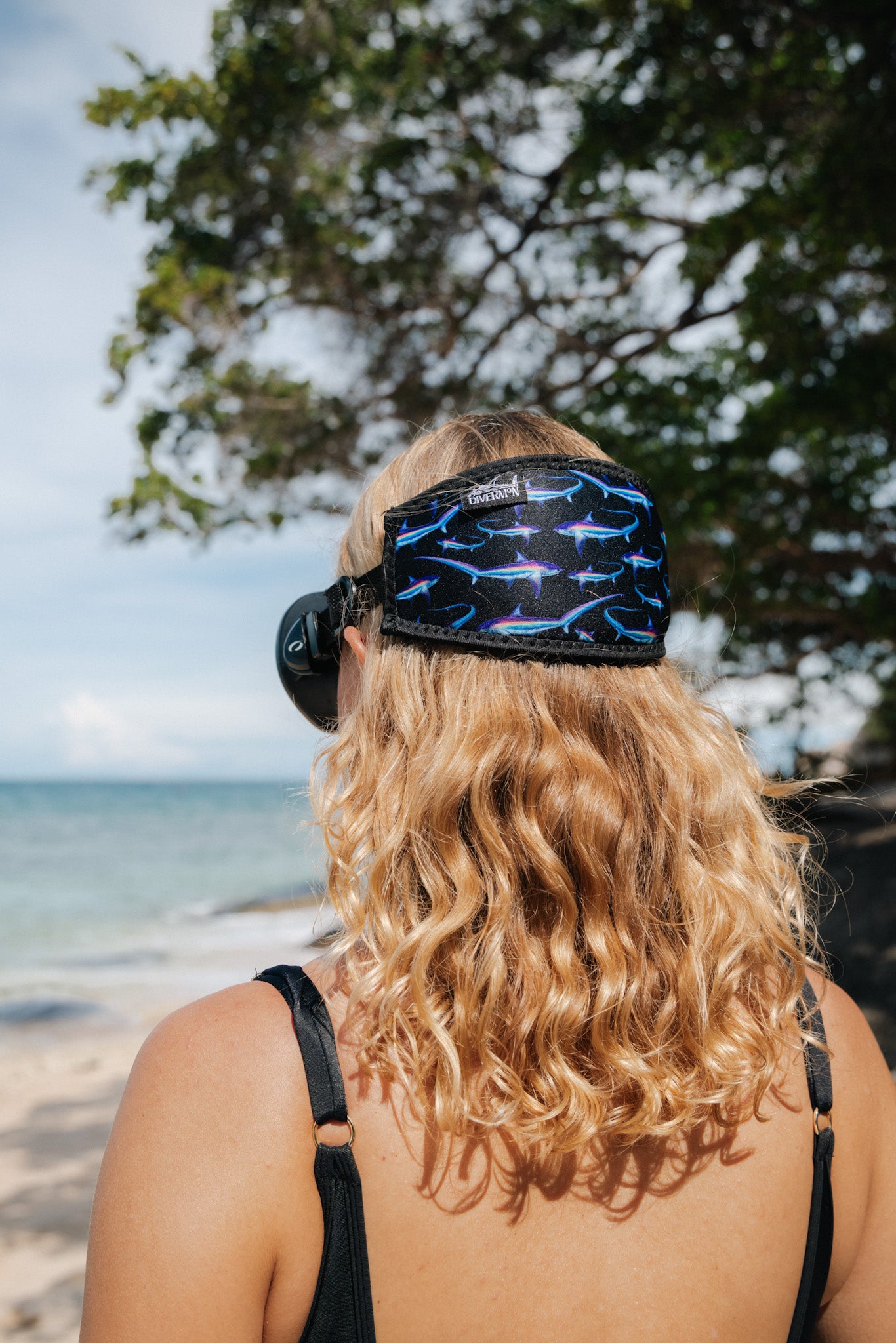 Blonde haired woman seen close up from behind at the beach with the black thresher design neoprene mask strap tamer ocean illustration by Diver Mon Art 