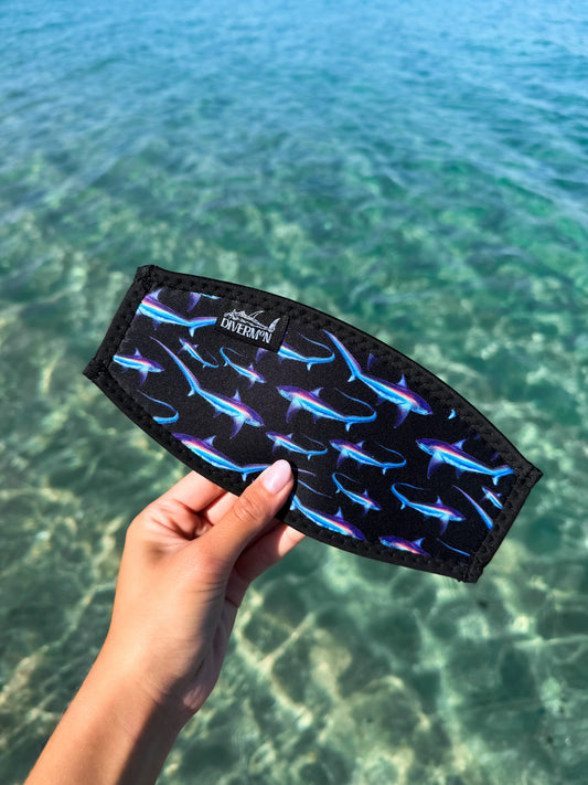 Hand holding the black thresher neoprene mask tamer design by Diver Mon Art design against a clear blue water background