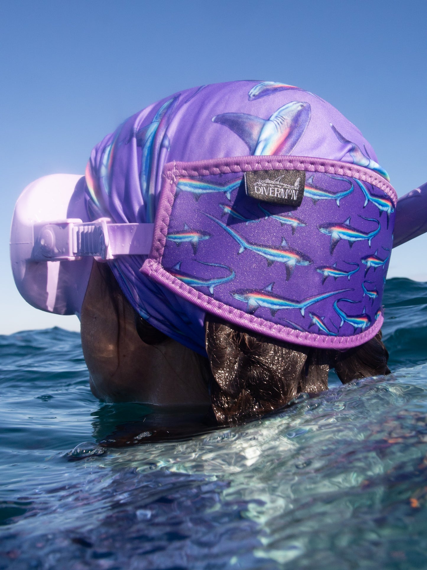 Dark haired woman seen close up behind in great detail above clear blue water wearing a purple mask fitted with the limited addition purple thresher neoprene mask tamer matching with the purple thresher UV gaiter ocean illustration by Diver Mon Art 