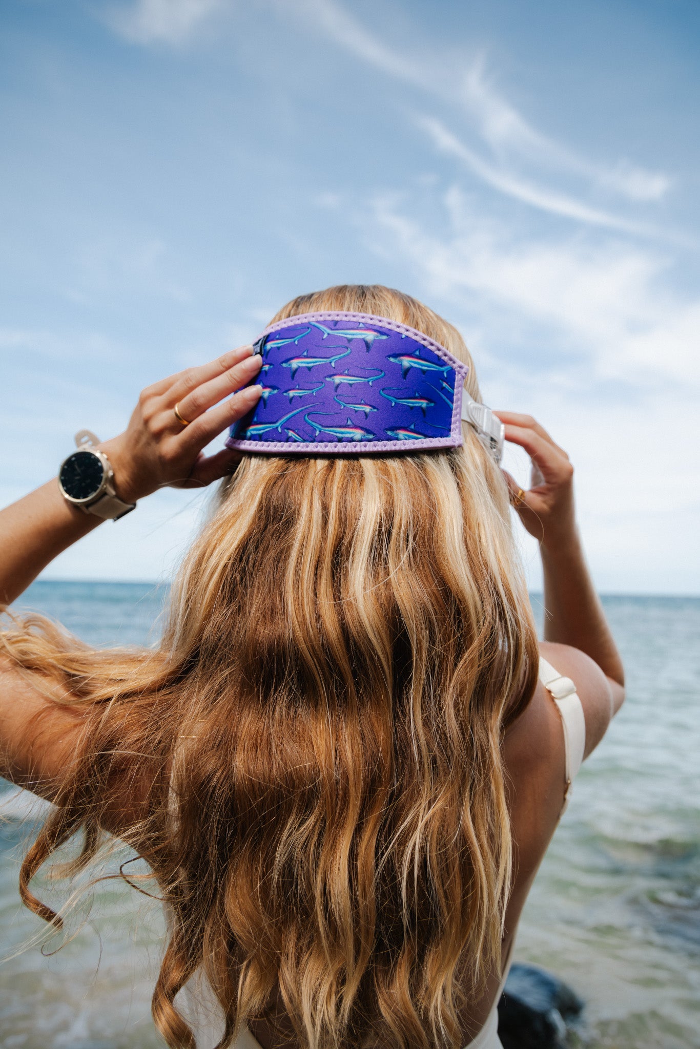 Blonde haired woman seen close up from behind at the shoreline at the beach in clear water with the purple thresher design neoprene mask strap tamer fitted to mask ocean illustration by Diver Mon Art 
