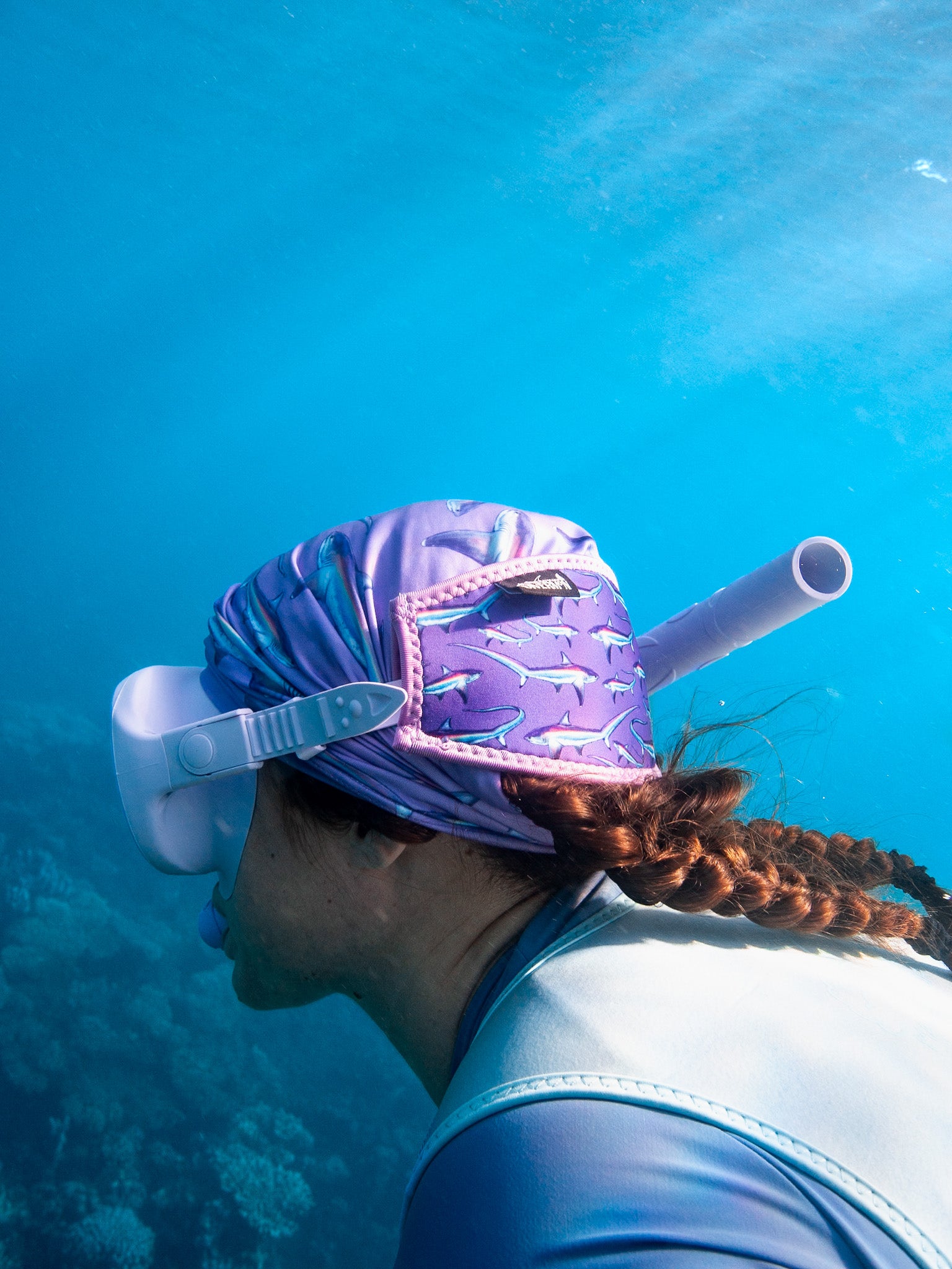 Dark haired women seen close up underwater in clear blue water wearing a mask fitted with the limited addition purple thresher neoprene mask strap tamer matching with the purple thresher UV gaiter ocean illustration by Diver Mon Art 