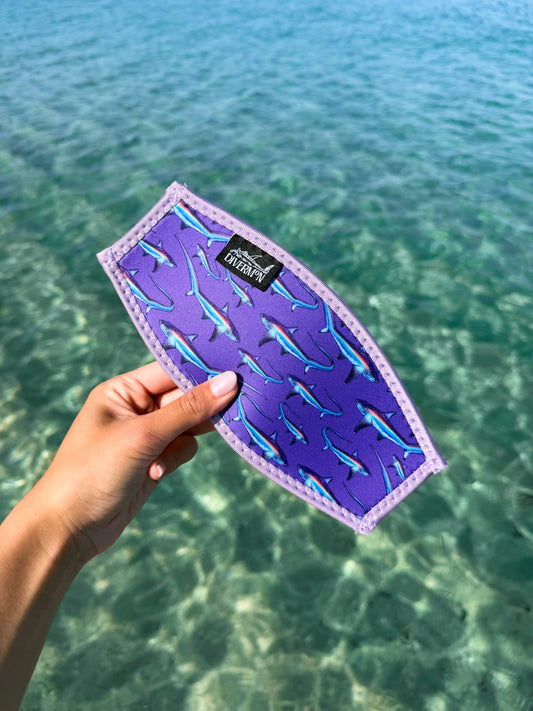Hand holding the purple thresher neoprene mask tamer design by Diver Mon Art design against a clear blue water background