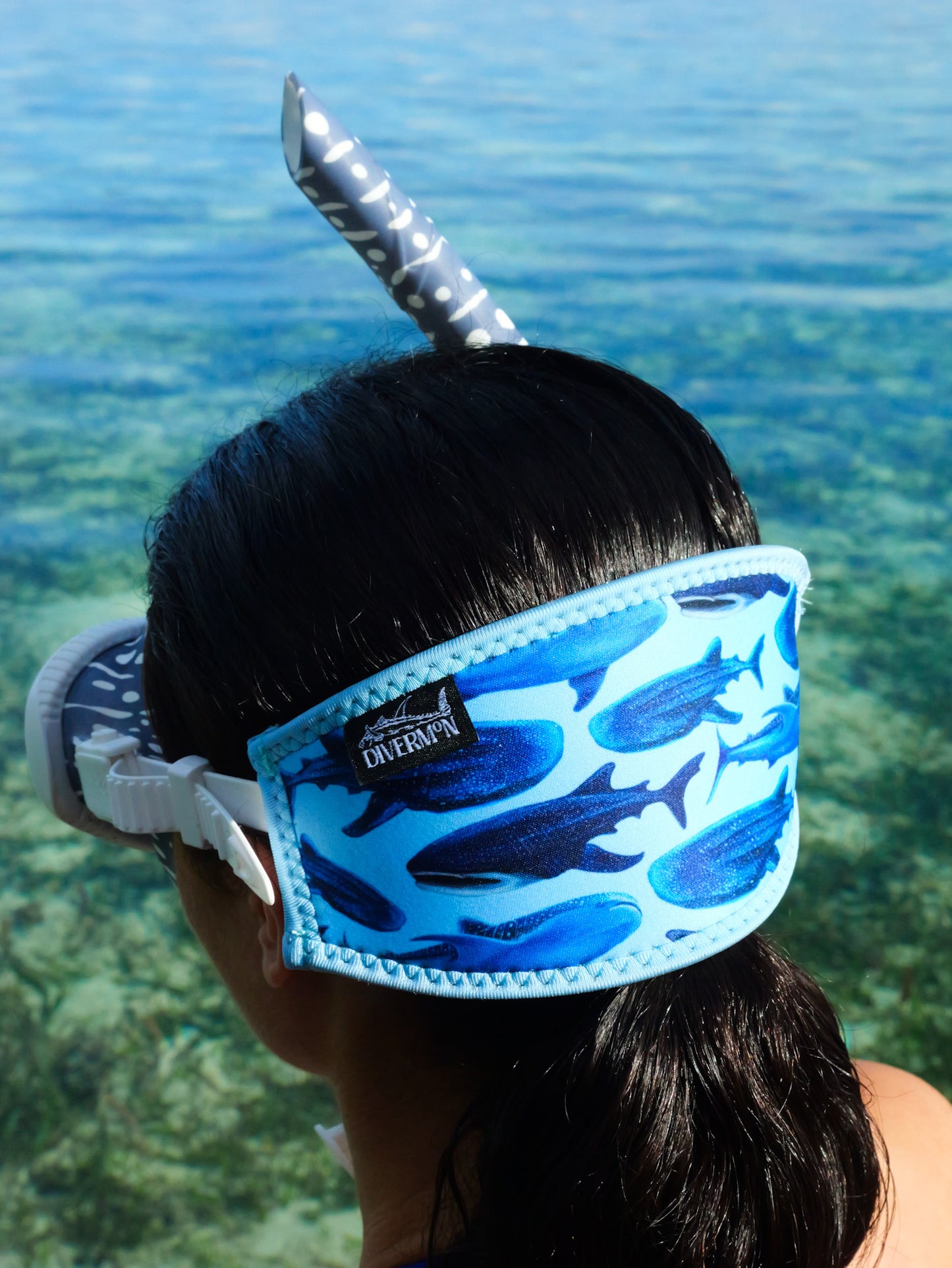 Dark haired woman seen close up side view in clear blue water whale shark design with blue background neoprene mask strap tamer in great detail fitted to mask ocean illustration by Diver Mon Art 
