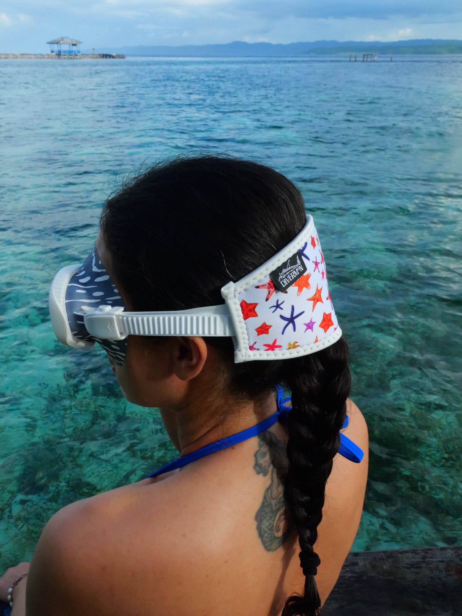 Dark haired woman shown from side view in blue clear water close up white sea star design neoprene mask strap tamer fitted to a mask ocean illustration by Diver Mon Art